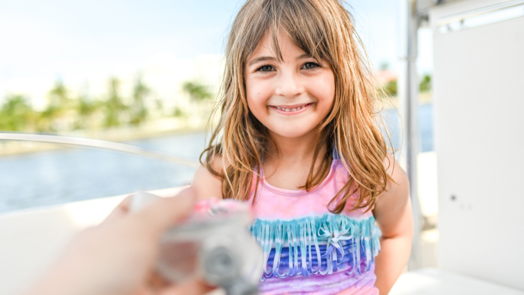  A young girl smiles as she holds a seashell close to the camera in front of her.